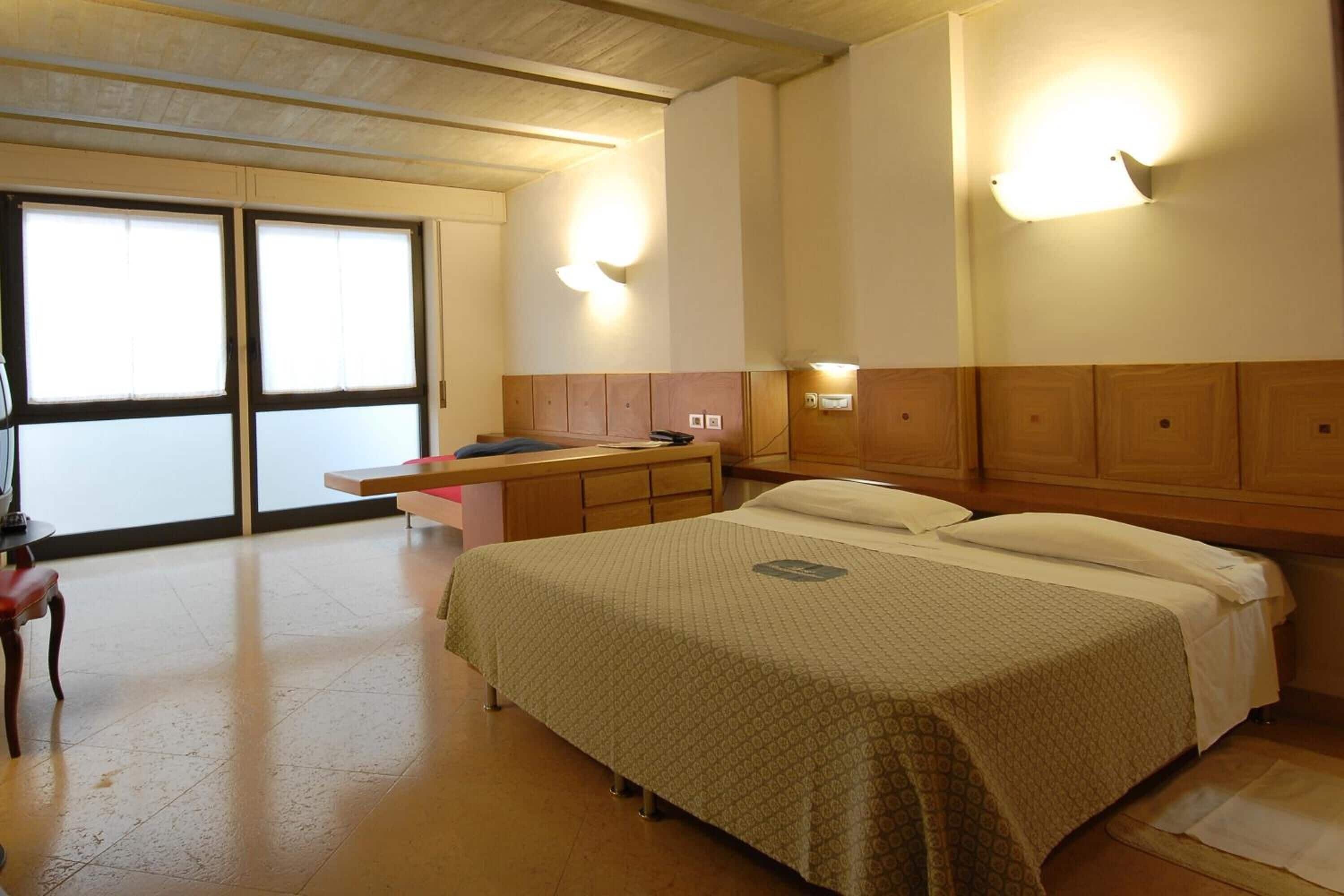 Una habitación de hotel con una cama, un escritorio, una silla y un ventanal grande.