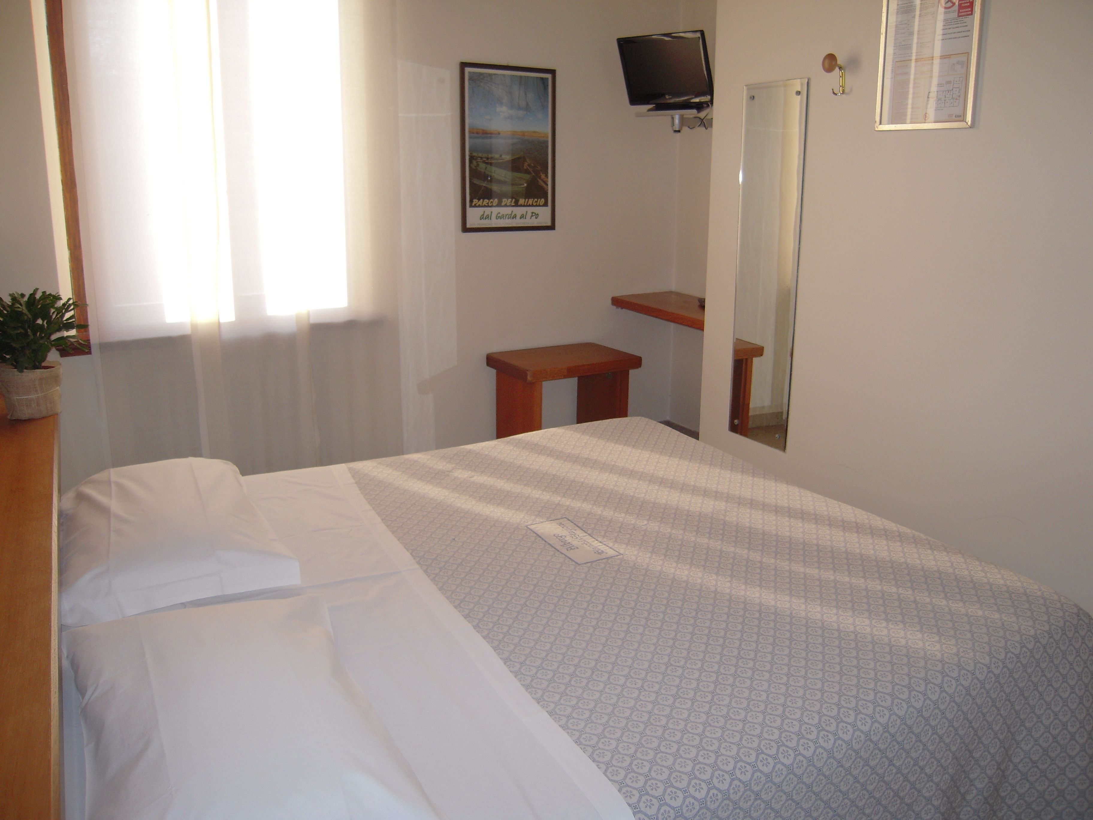 A bedroom with a bed, a small wooden table, a television mounted on the wall, and a framed picture.
