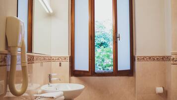 A bathroom with a sink, toilet, and a window with open shutters.