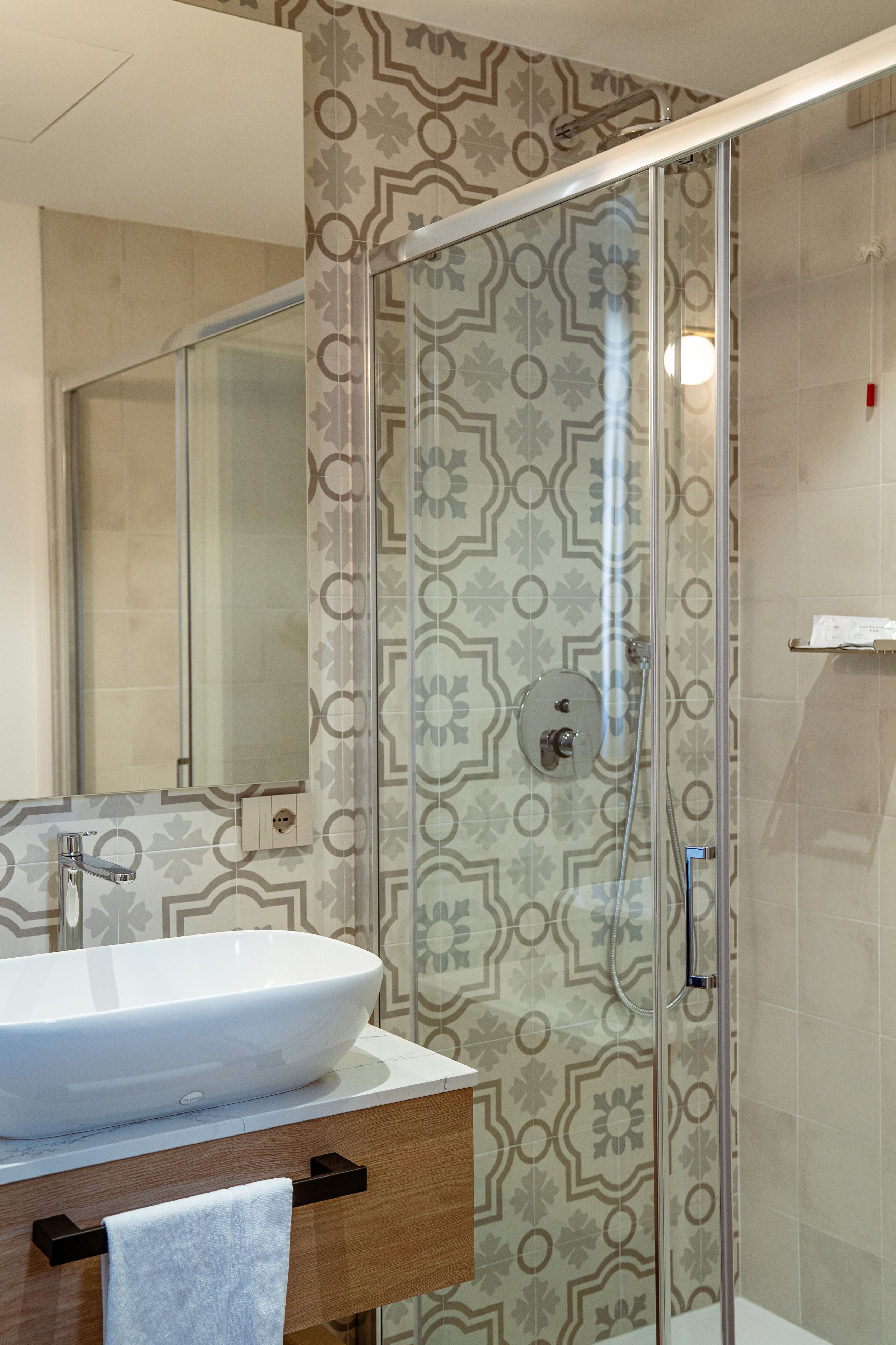 A modern bathroom with a glass-enclosed shower, a white sink, and patterned wall tiles.