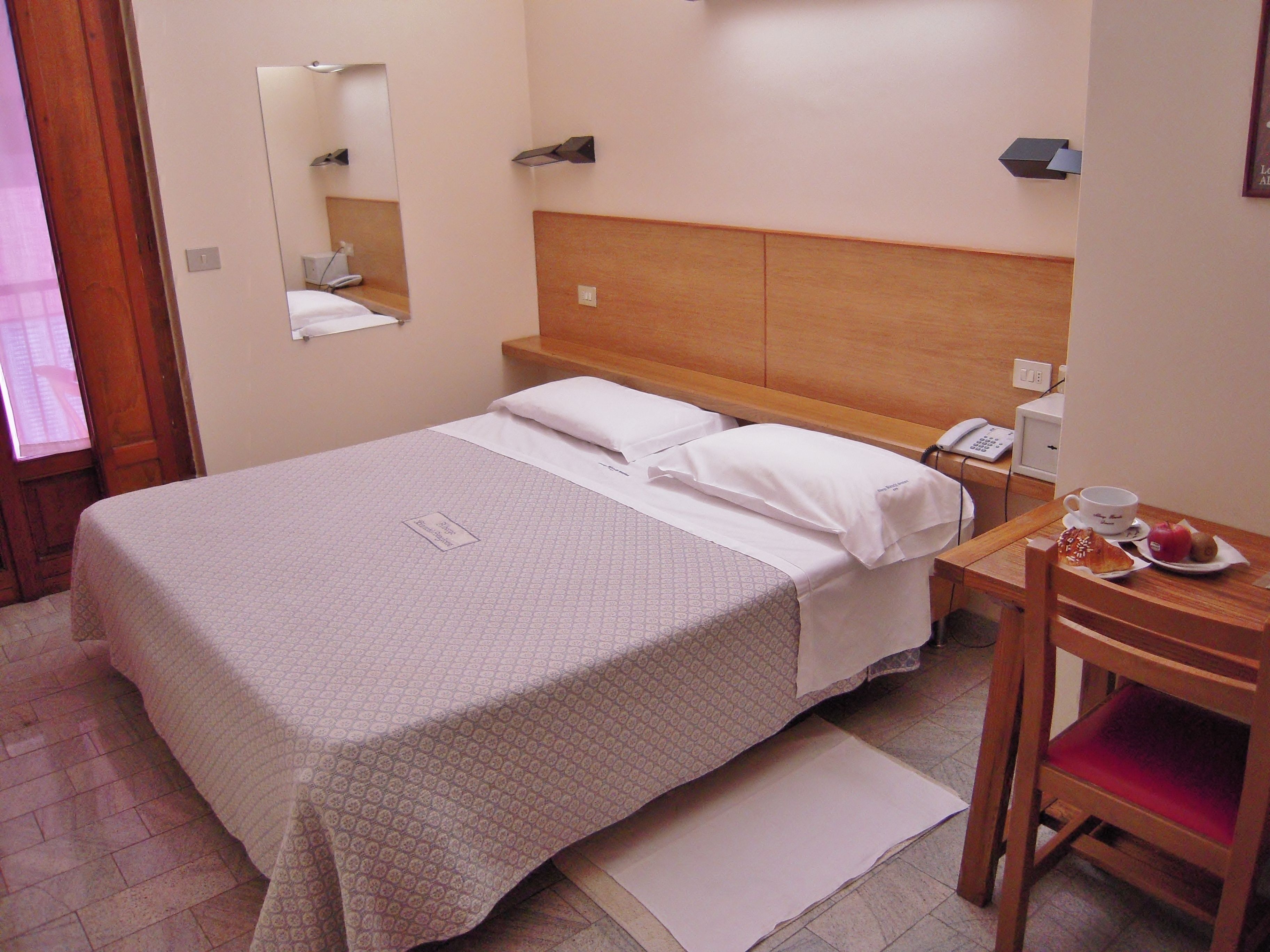 A hotel room with a bed, bedside table, and a chair.