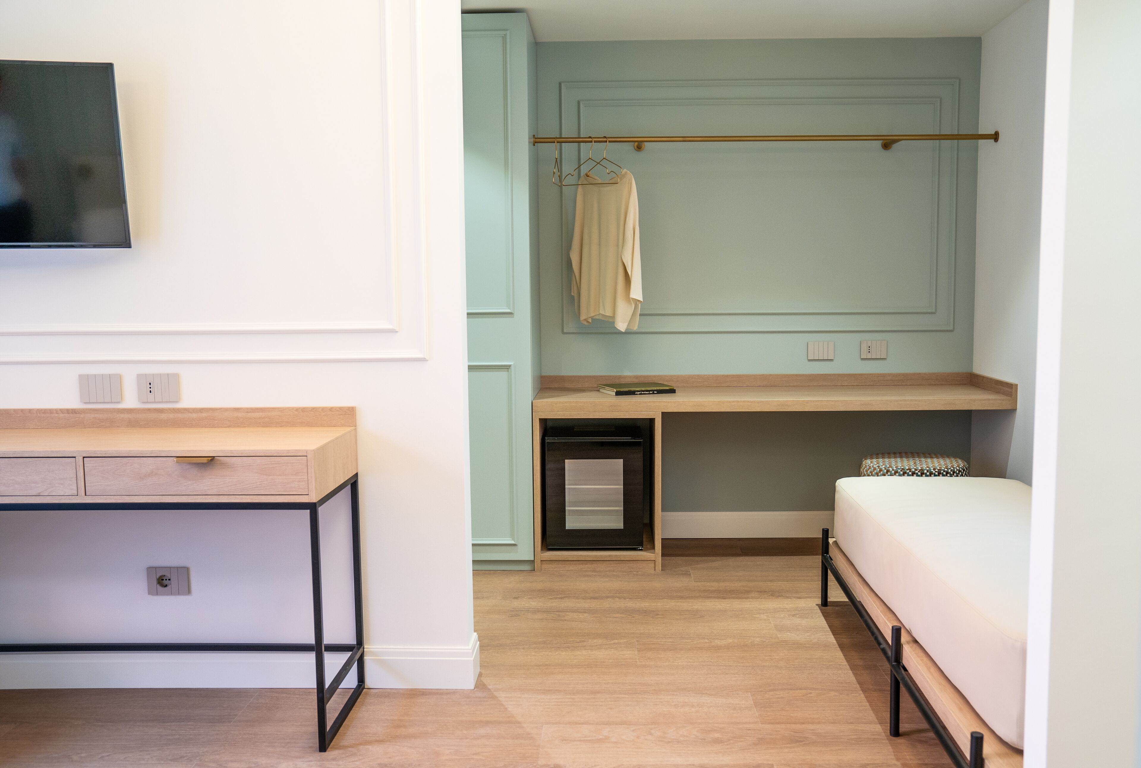A room with a bed, a desk, a TV, and a coat rack.