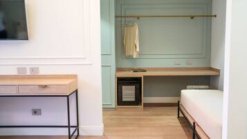 A room with a bed, a desk, a TV, and a coat rack.