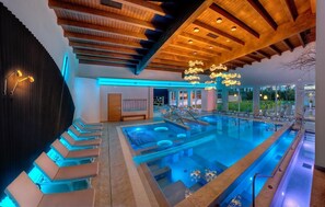 A modern indoor pool area with tiered seating and a ceiling with exposed beams. - Eliseo Terme (Montegrotto Terme)
