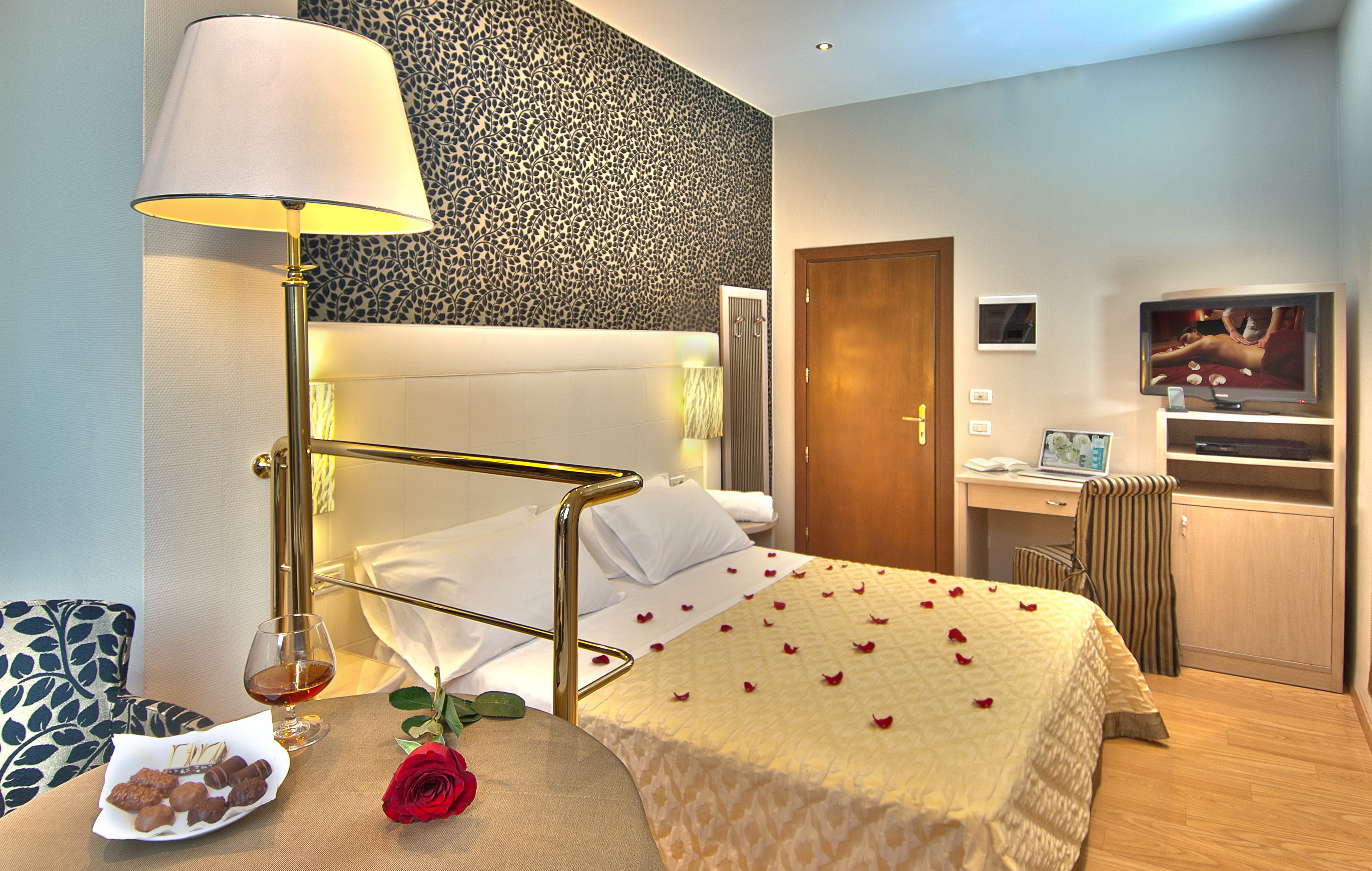 A hotel room with a bed, bedside table, lamp, and a TV.