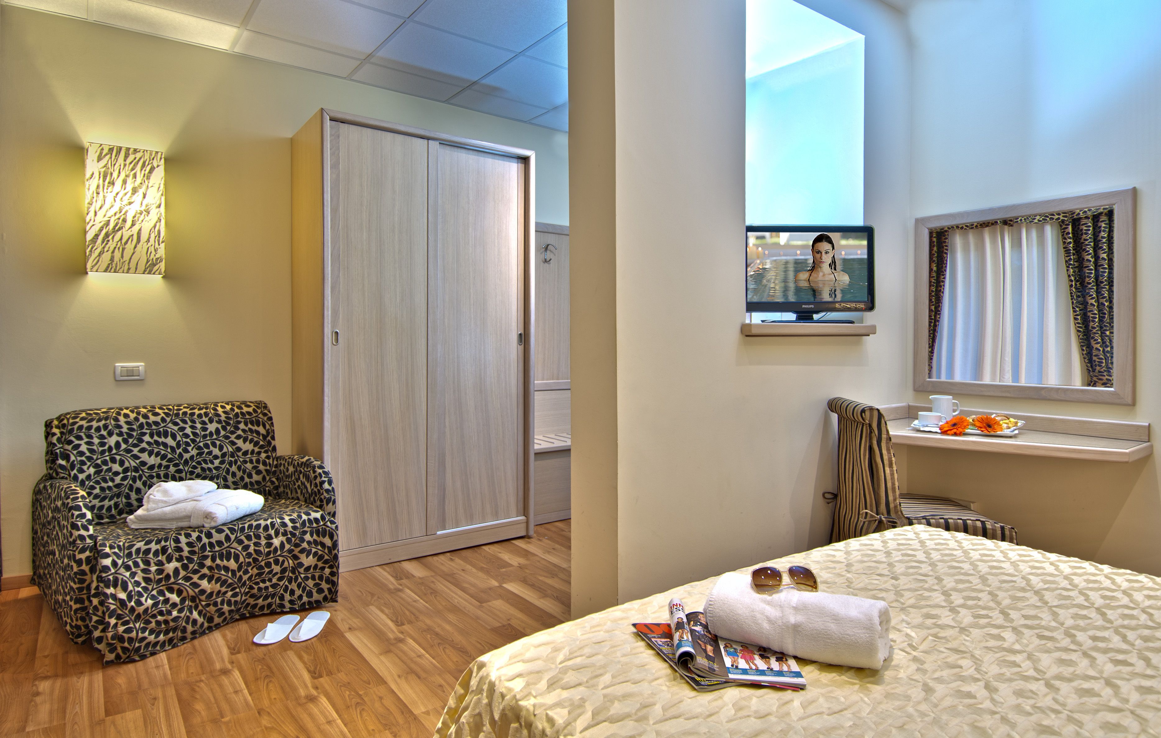 Een hotelkamer met een slaapbank, een bed, een televisie en een raam met gordijnen.