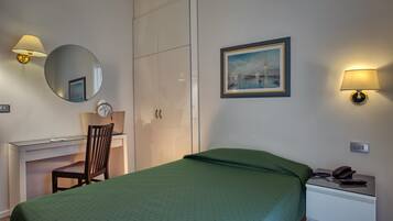 Habitación de hotel con cama, escritorio con silla, armario, mesita de noche con teléfono y lámpara de pared.