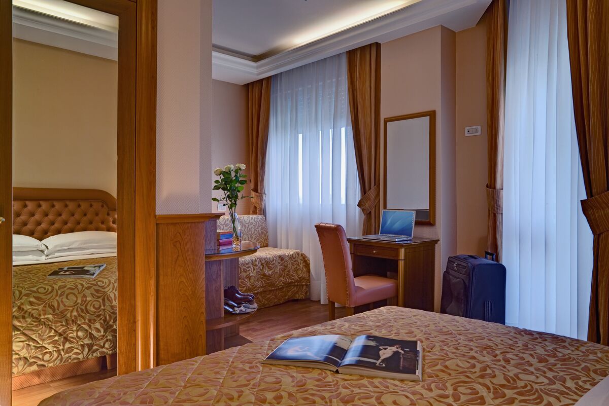 A hotel room with a large bed, a desk with a laptop, a chair, and a suitcase.
