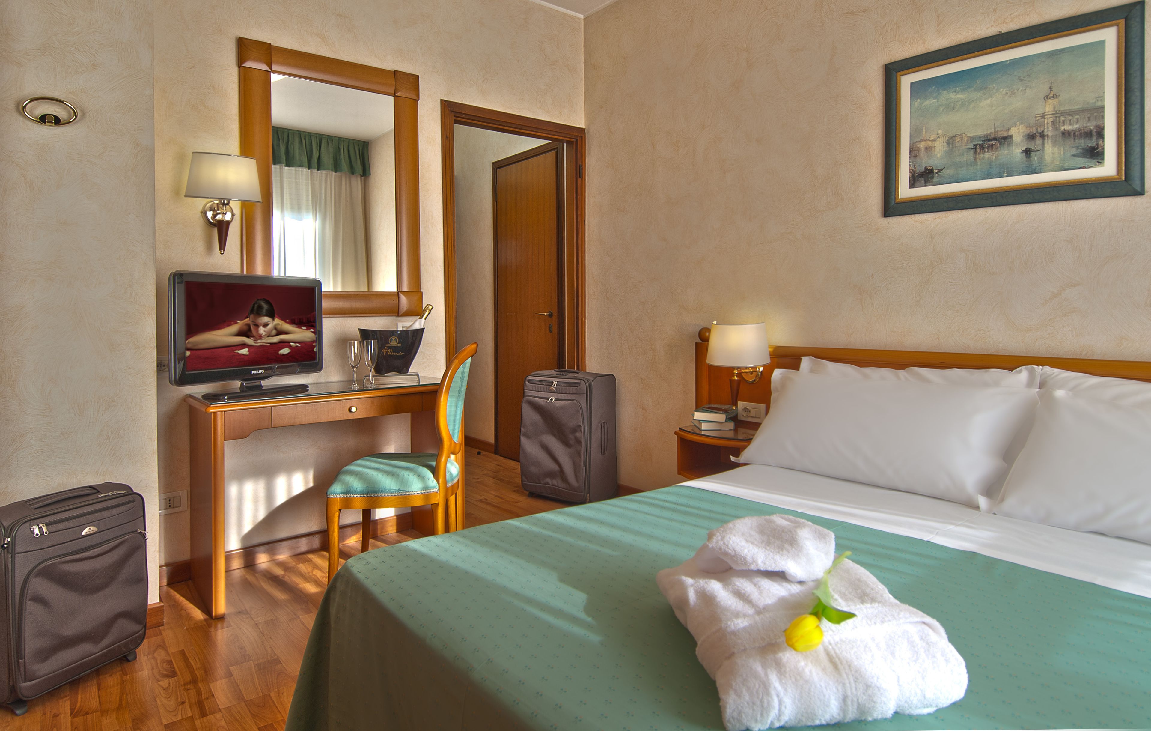 A hotel room with a bed, desk, chair, television, and a painting on the wall.