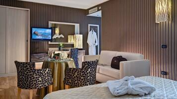 A hotel room with a bed, a TV, a sofa, and a dining area with chairs and a table.