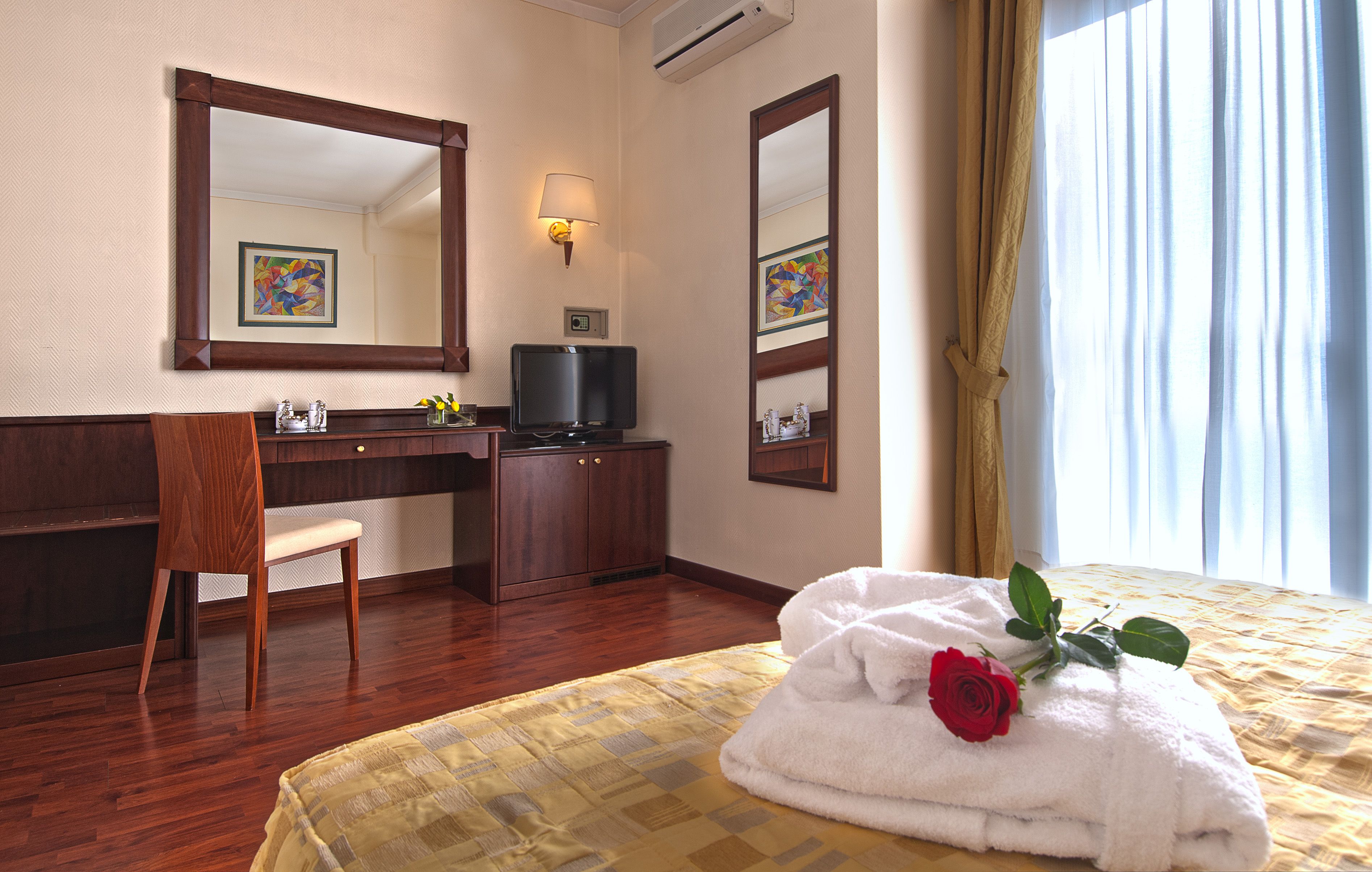 A hotel room with a bed, a desk, a chair, a television, and a window with curtains.