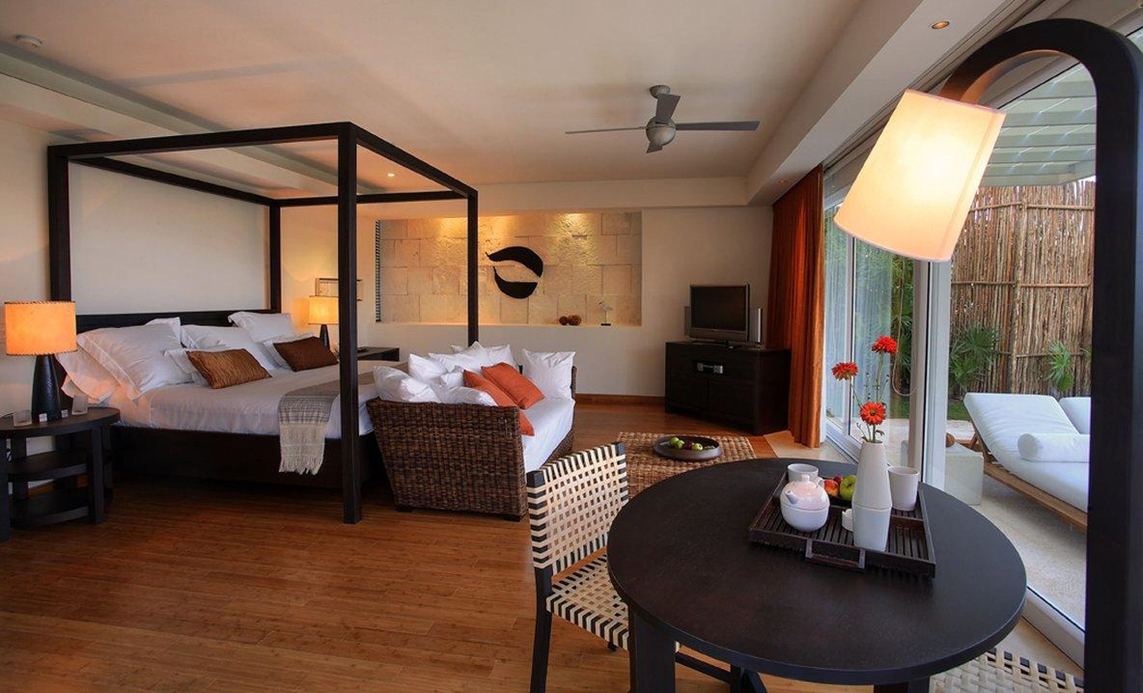 Quarto de hotel moderno com cama de dossel, área de refeições com mesa redonda e uma grande janela com vista para o exterior.