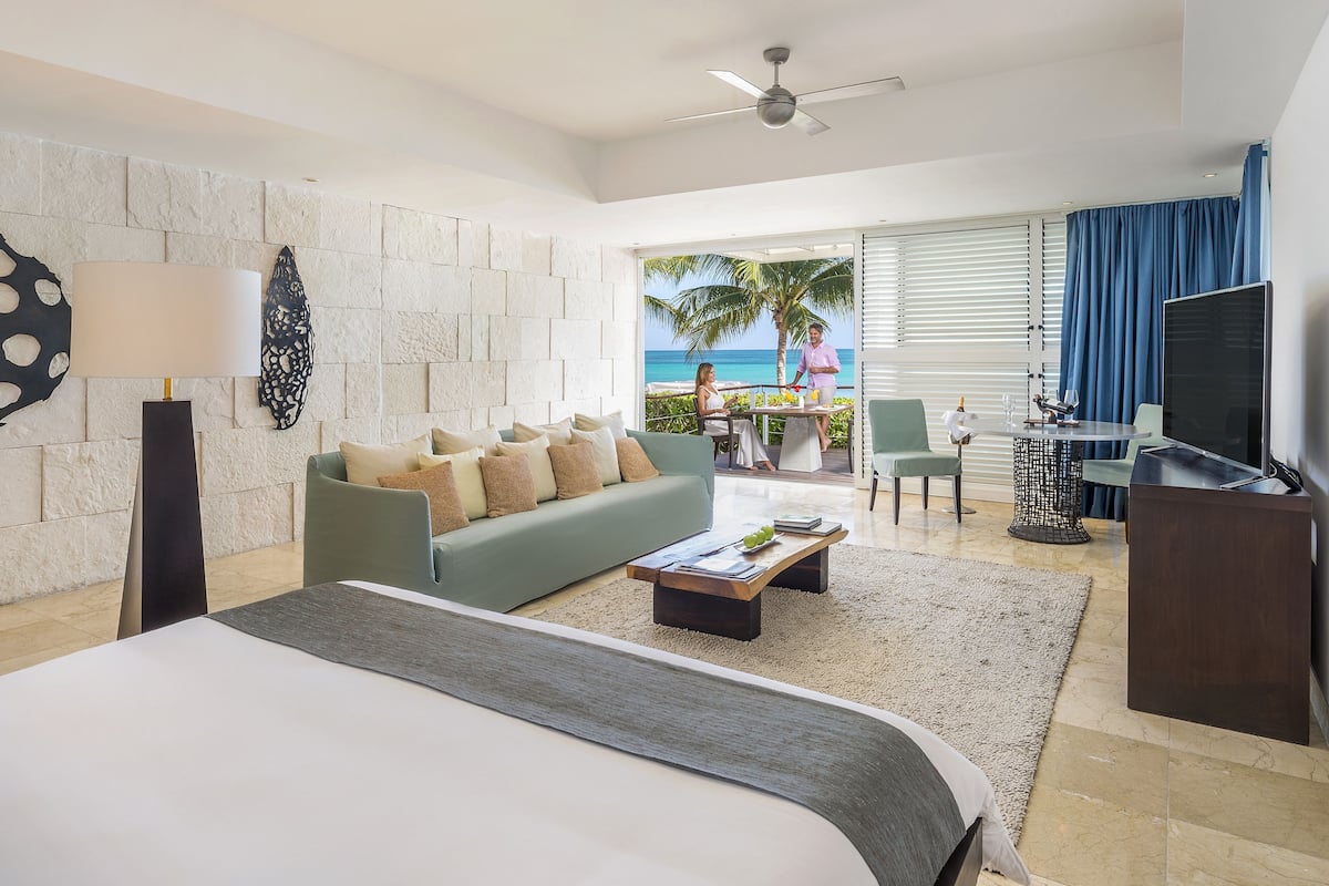 Une chambre d’hôtel moderne dotée d’un grand lit, d’un canapé, d’un bureau et d’un balcon offrant une vue sur l’océan.