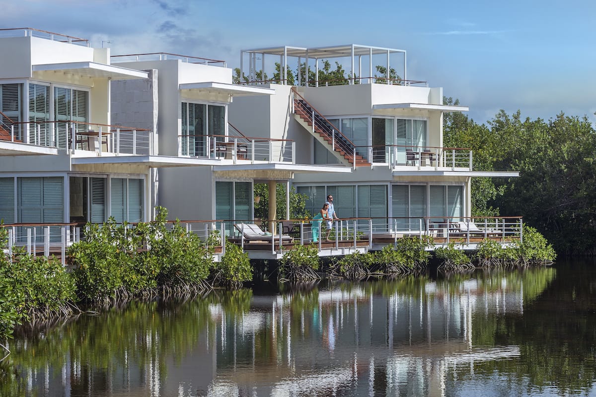 Une propriété moderne à plusieurs étages, située au bord de l’eau, dotée de balcons, d’un escalier et offrant une vue sur l’eau.