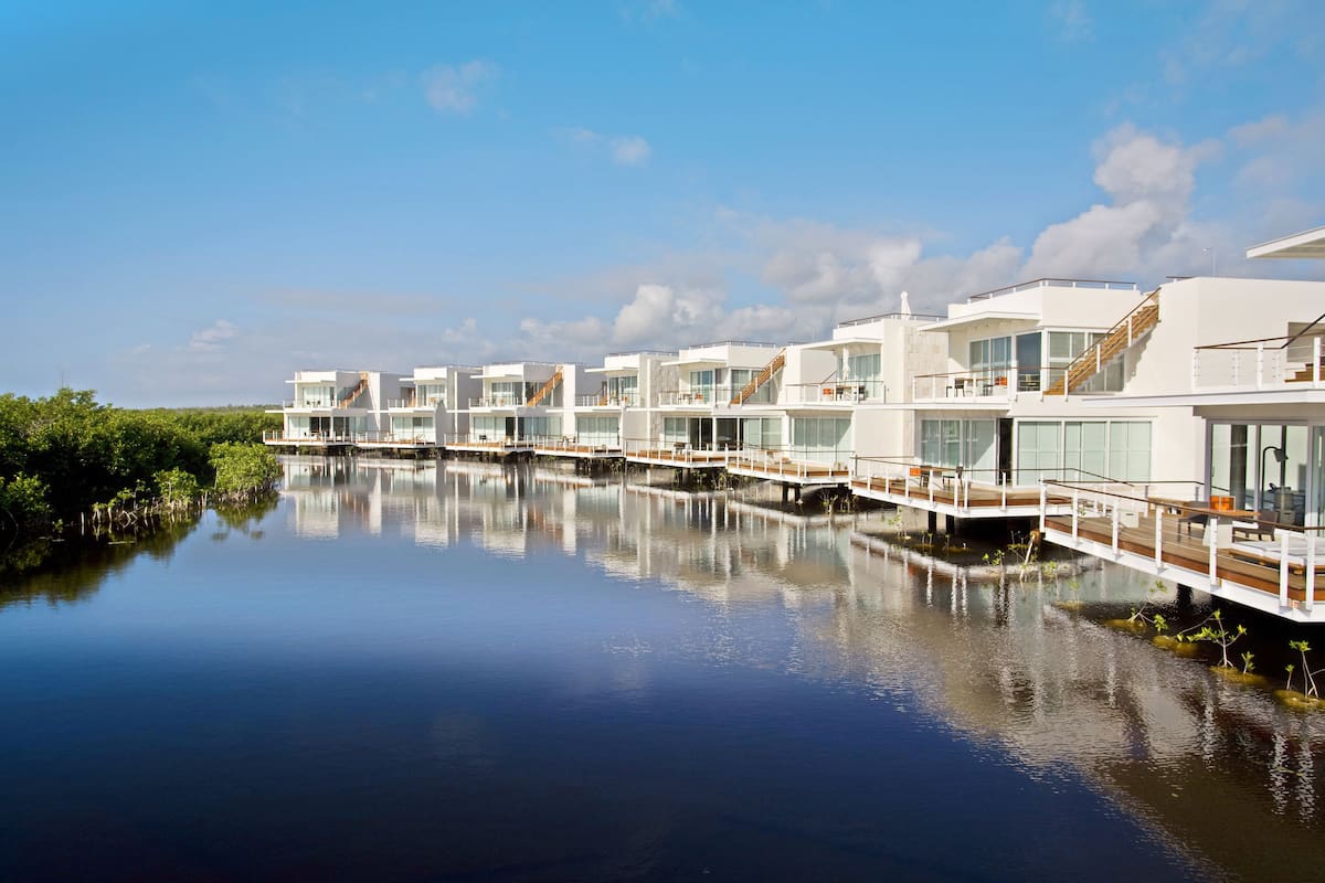 Un hôtel situé au bord de l’eau, composé de plusieurs bâtiments modernes reliés par des ponts, et offrant une vue sur l’eau et la végétation environnante.