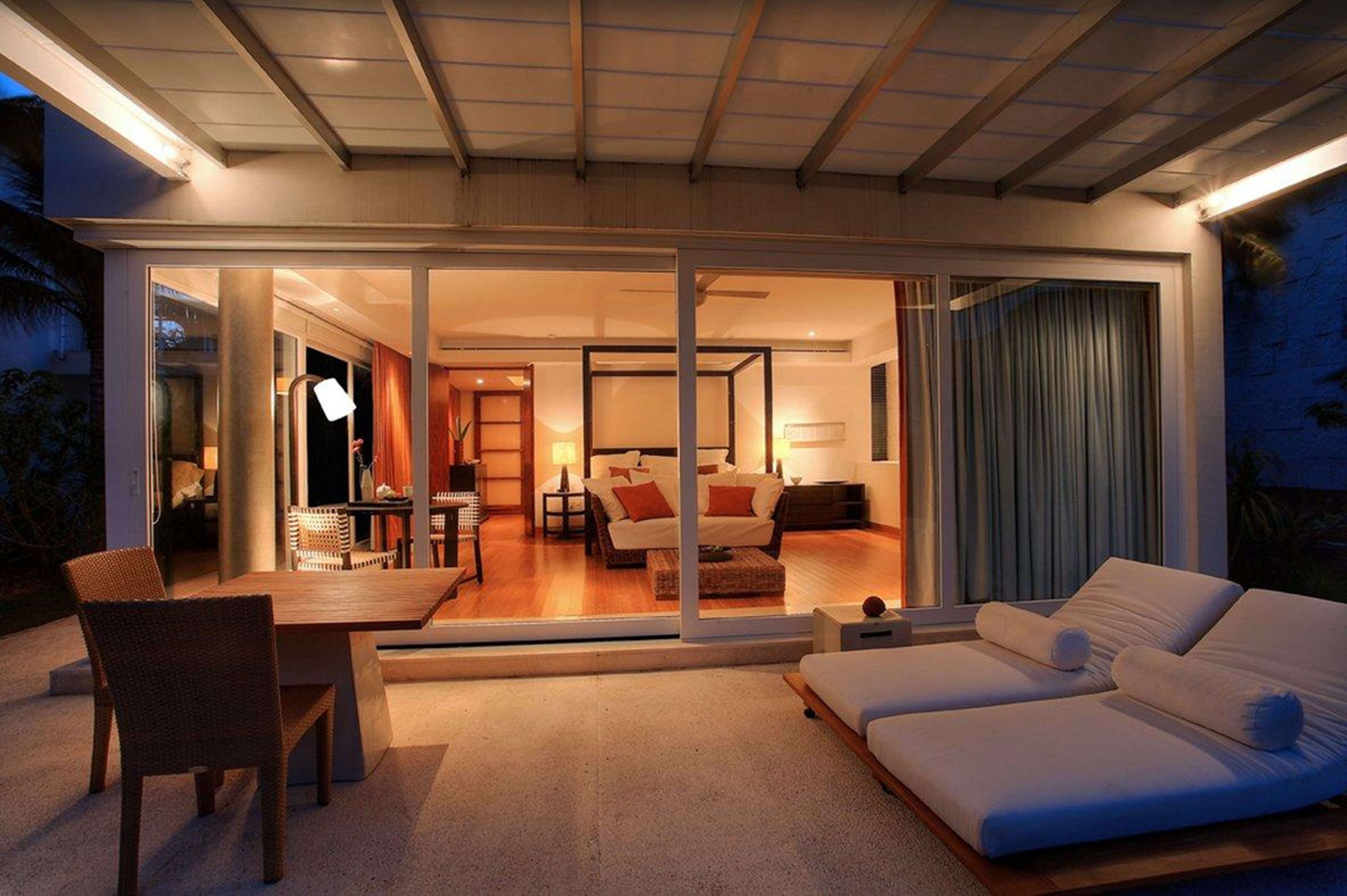 Un interior moderno con comedor, sala de estar con sofá y televisor, y un dormitorio con cama y cortinas.
