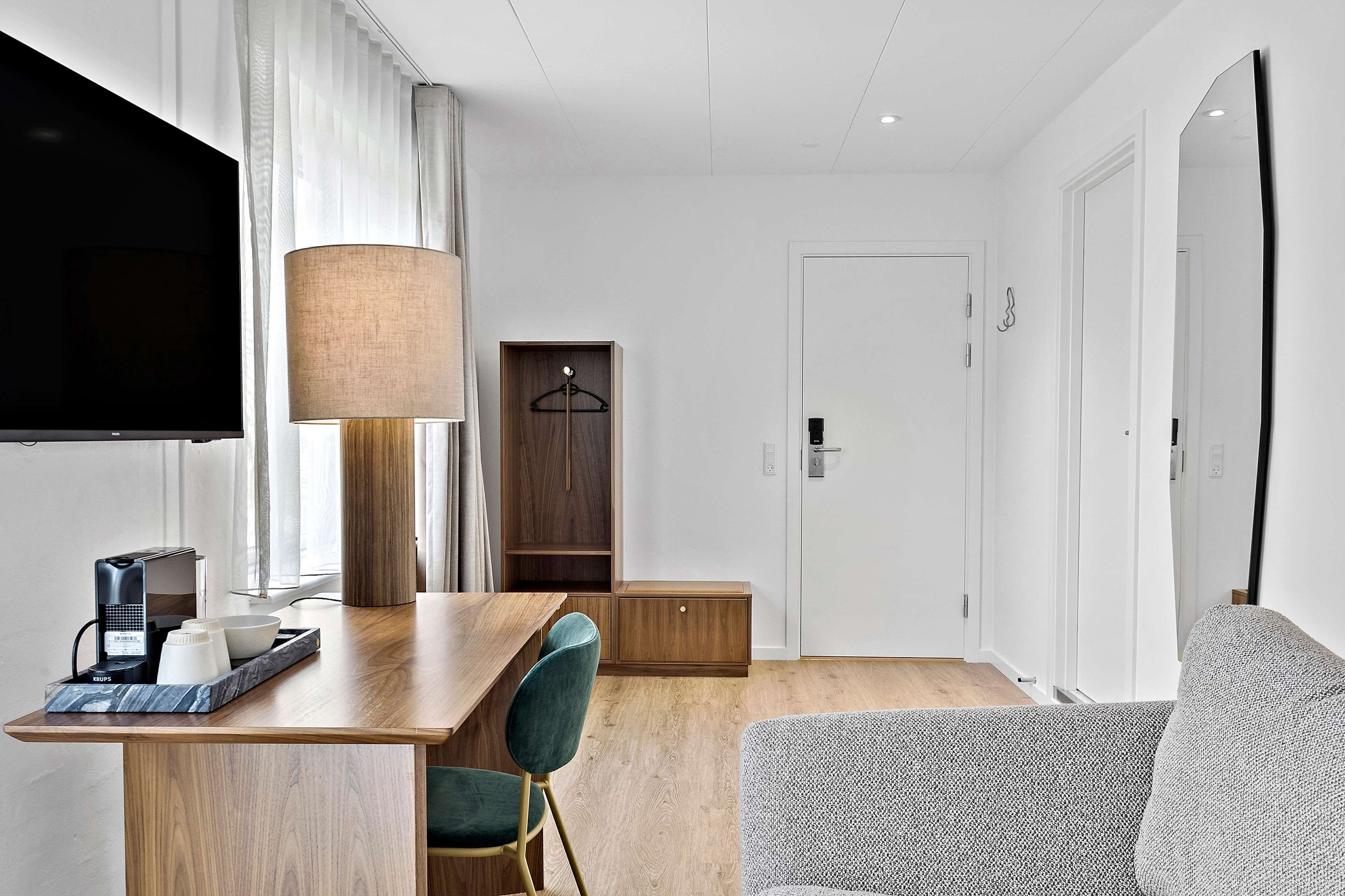 Een moderne hotelkamer met een houten bureau, een televisie, een lamp, een bank en een kledingkast.