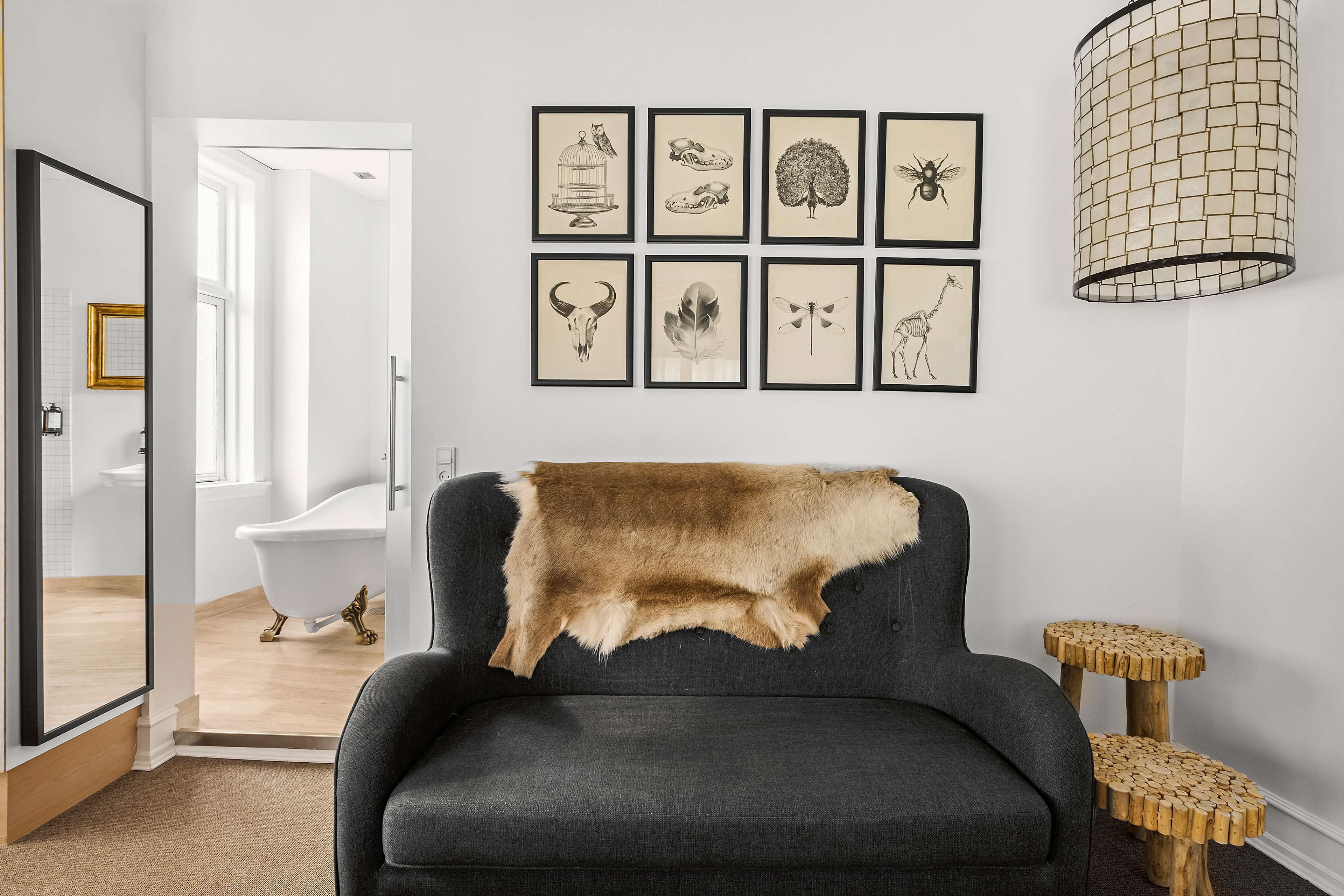 Una stanza con una poltrona antracite, una coperta in pelliccia e una parete con illustrazioni in bianco e nero incorniciate.