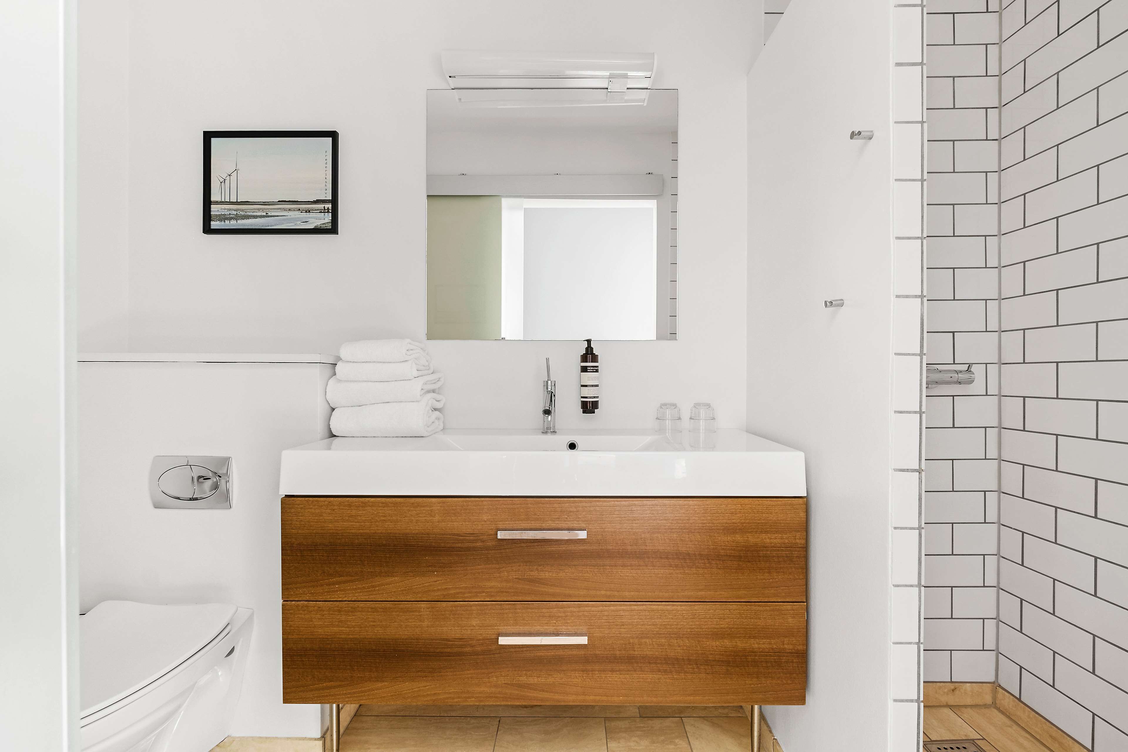 A modern bathroom with a white sink, wooden vanity, and a large mirror.