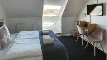 A hotel room with a bed, a desk, a chair, a TV, and a window with a view of buildings.