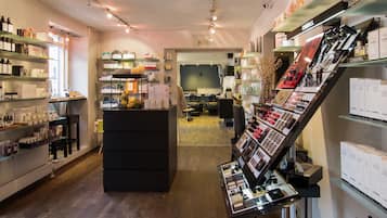 Tienda minorista bien iluminada con estantes llenos de diversos productos, un mostrador de exhibición con cosméticos y un área de descanso al fondo.