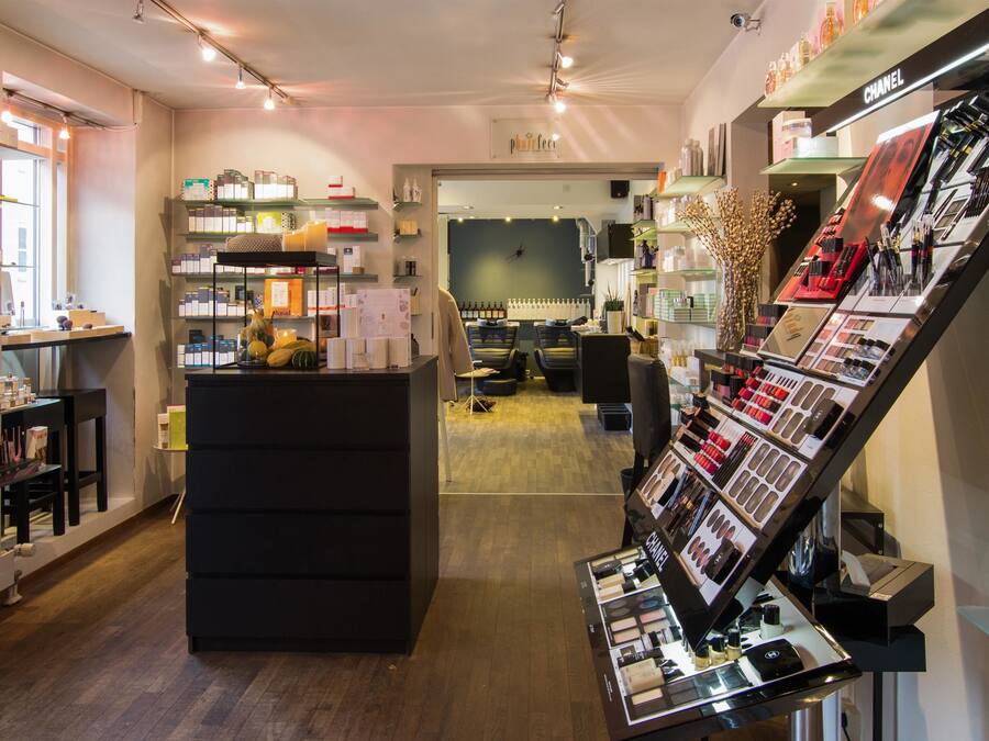 Tienda minorista bien iluminada con estantes llenos de diversos productos, un mostrador de exhibición con cosméticos y un área de descanso al fondo.