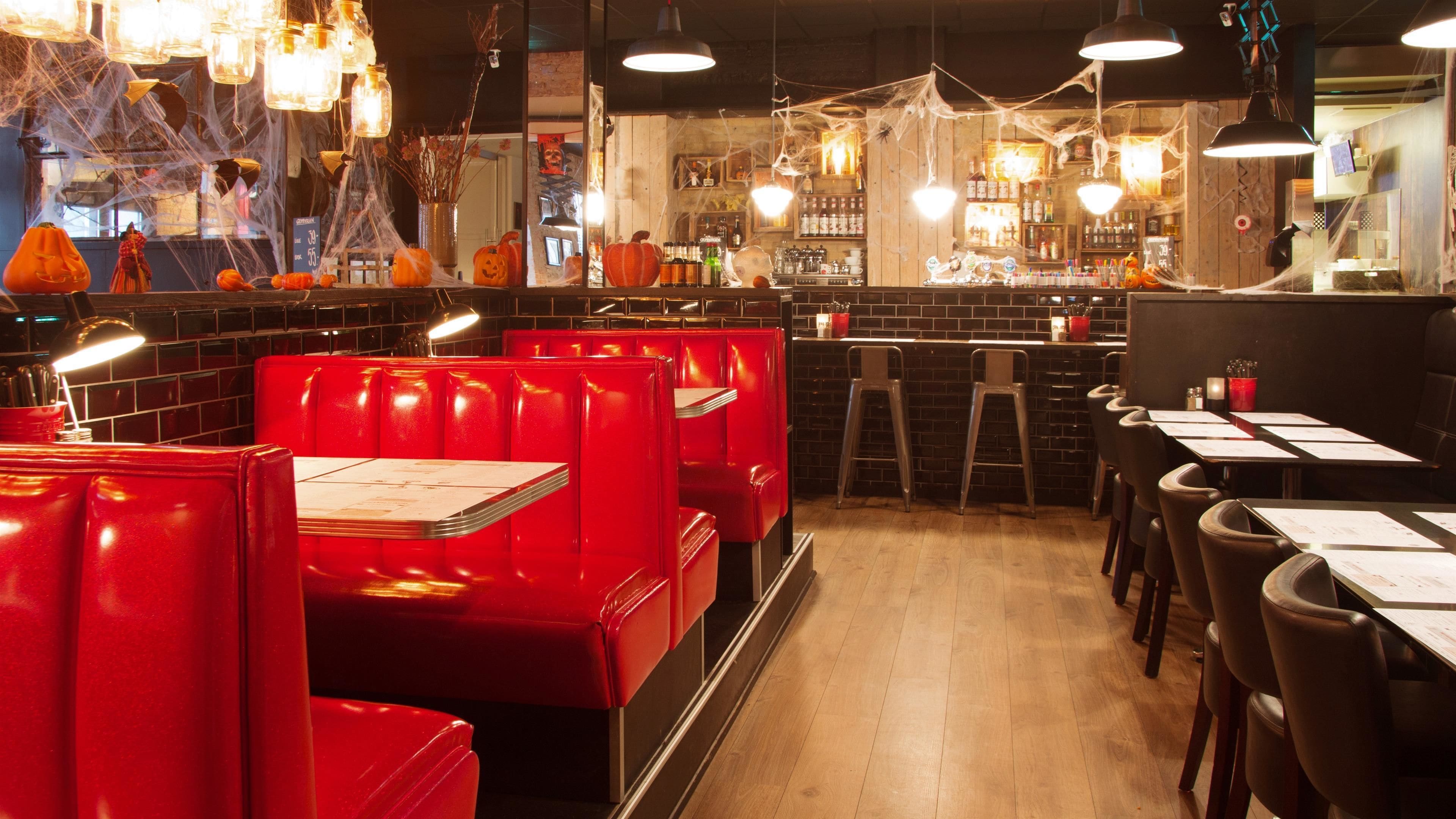 Interior de restaurante con cabinas rojas, suelo de madera y una zona de bar con botellas y vasos.