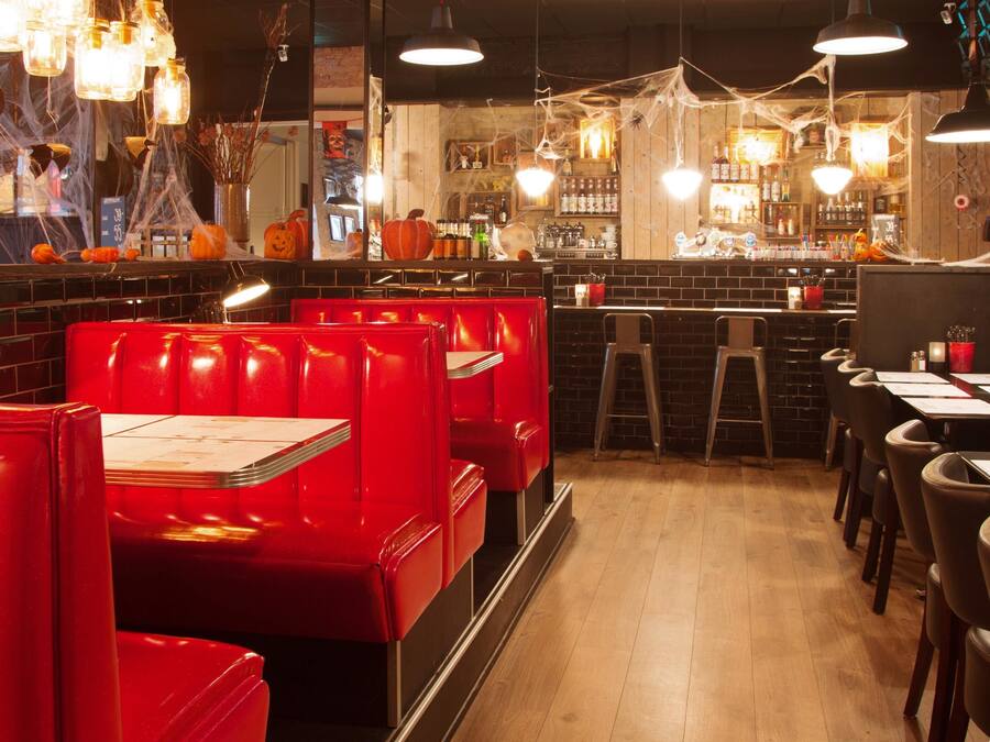 Interior de restaurante con cabinas rojas, suelo de madera y una zona de bar con botellas y vasos.