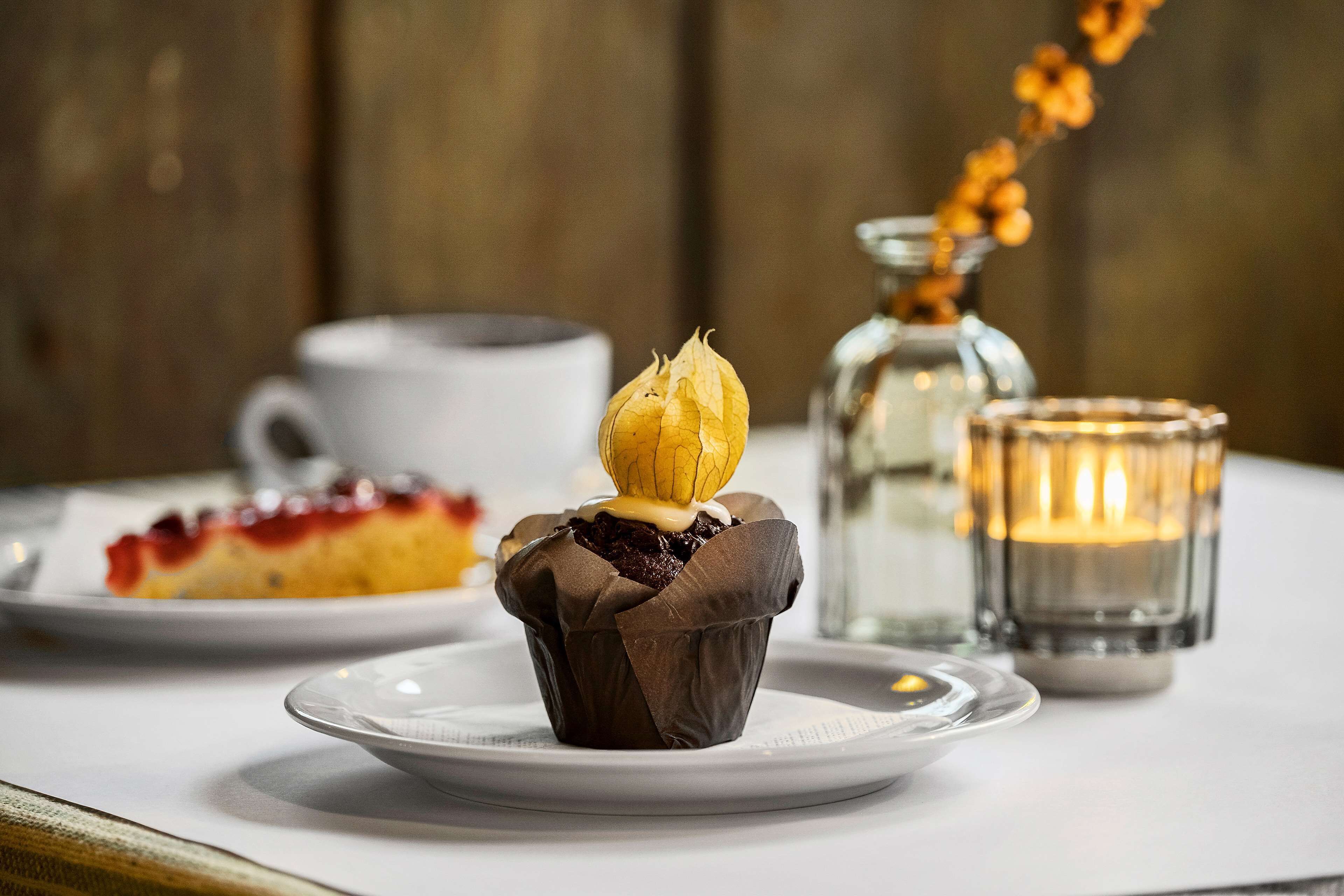 Une table de desserts avec un petit gâteau au chocolat, une bougie dans un verre et une assiette blanche sur laquelle est posée une part de gâteau.