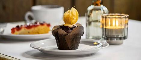 Une table de desserts avec un petit gâteau au chocolat, une bougie dans un verre et une assiette blanche sur laquelle est posée une part de gâteau.