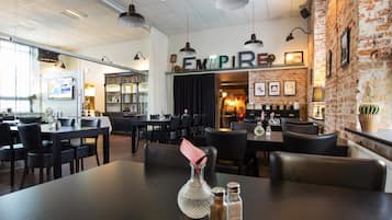 L’intérieur d’un restaurant avec un mur en briques, des chaises en cuir noir et une enseigne « EMPIRE ».