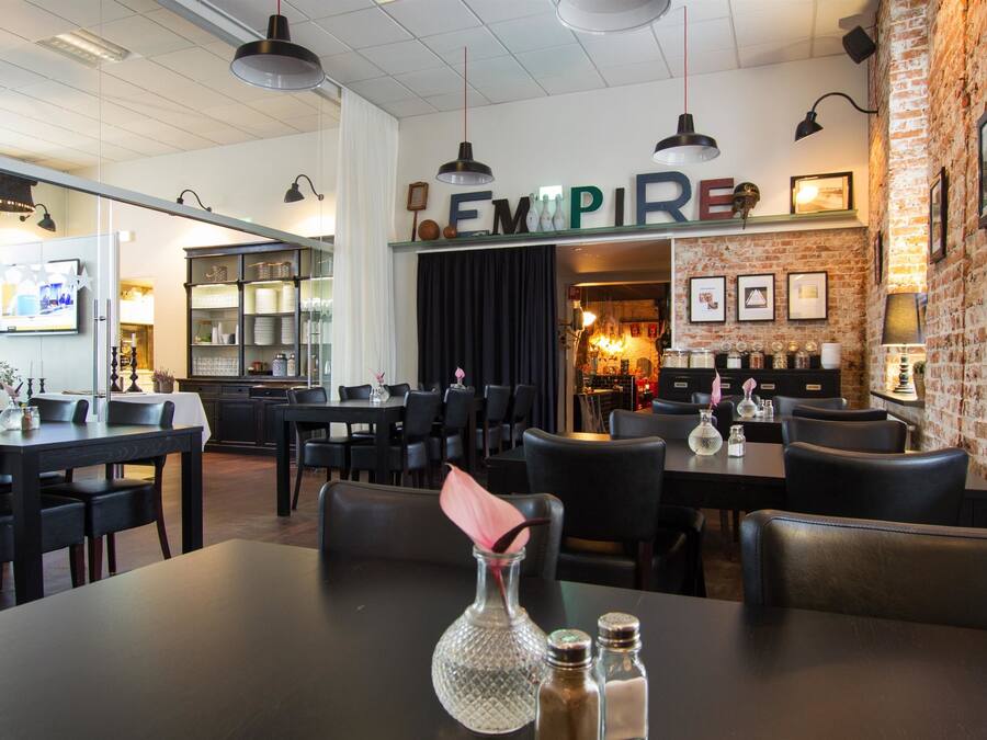 L’intérieur d’un restaurant avec un mur en briques, des chaises en cuir noir et une enseigne « EMPIRE ».
