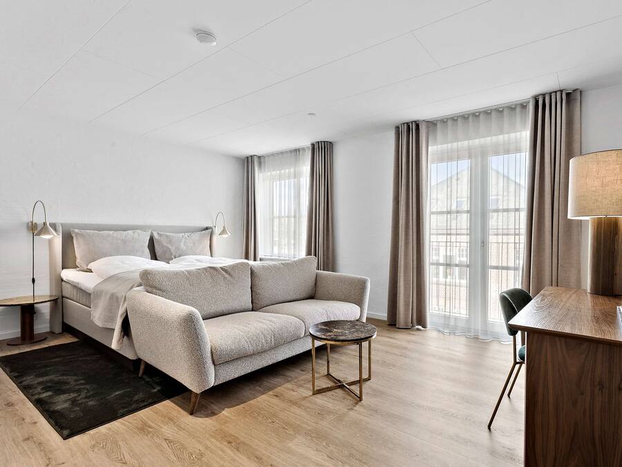 A modern hotel room with a bed, a sofa, a desk, and a lamp.