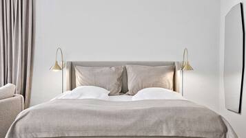 A neatly made bed with a neutral-colored duvet, two bedside lamps, and a chair to the left.