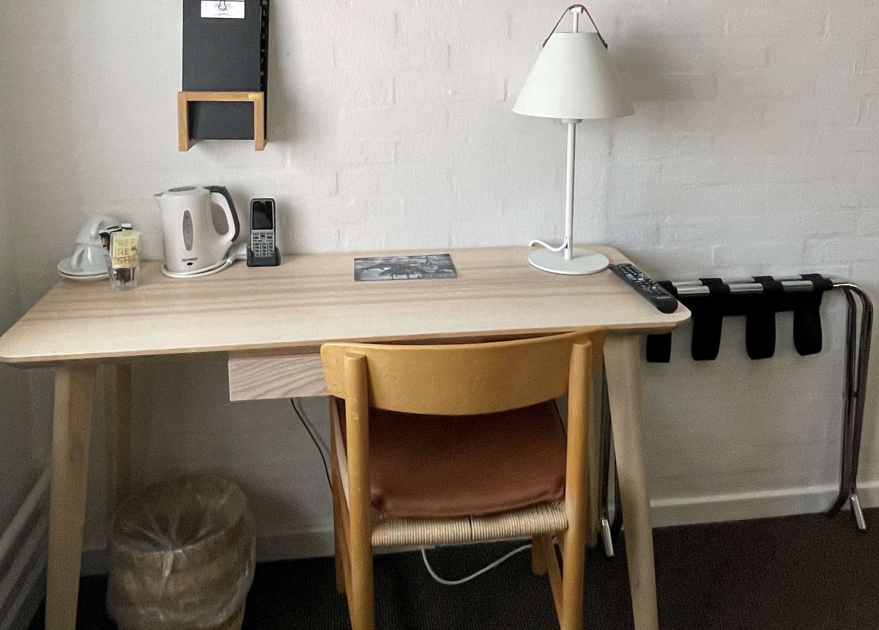 Un espacio de trabajo pequeño y ordenado, con un escritorio, una silla, una lámpara y diversos útiles de oficina.