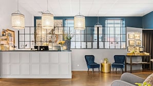 Un moderno vestíbulo de hotel con una recepción, dos sillones azules y un sofá gris.