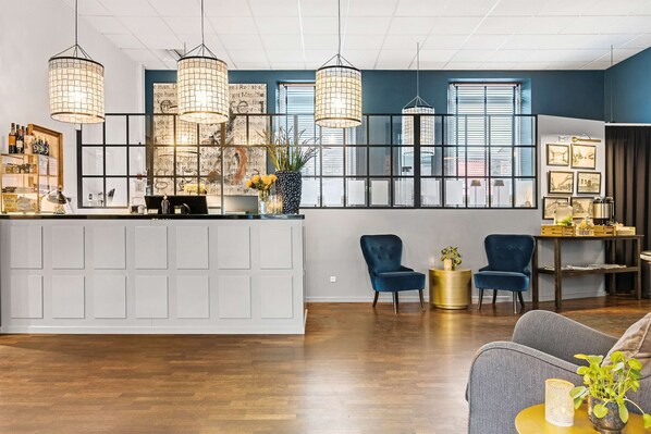 A modern hotel lobby with a reception desk, two blue armchairs, and a grey sofa. - Best Western Hotel Herman Bang (Frederikshavn)