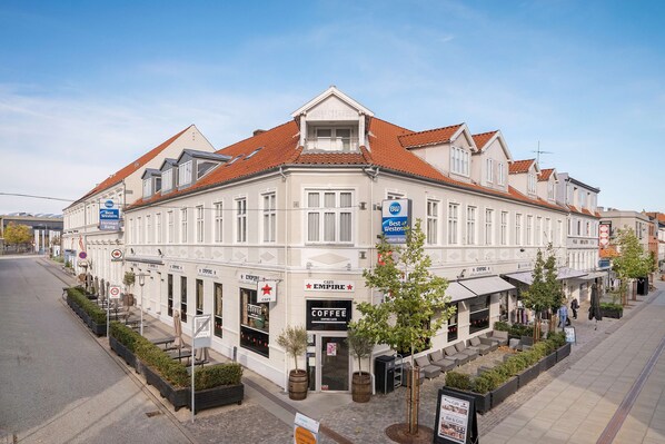 A white building with a red-tiled roof, storefronts labeled 'Best Western' and 'Coffee Empire', and outdoor seating areas with potted plants. - Best Western Hotel Herman Bang (Frederikshavn)