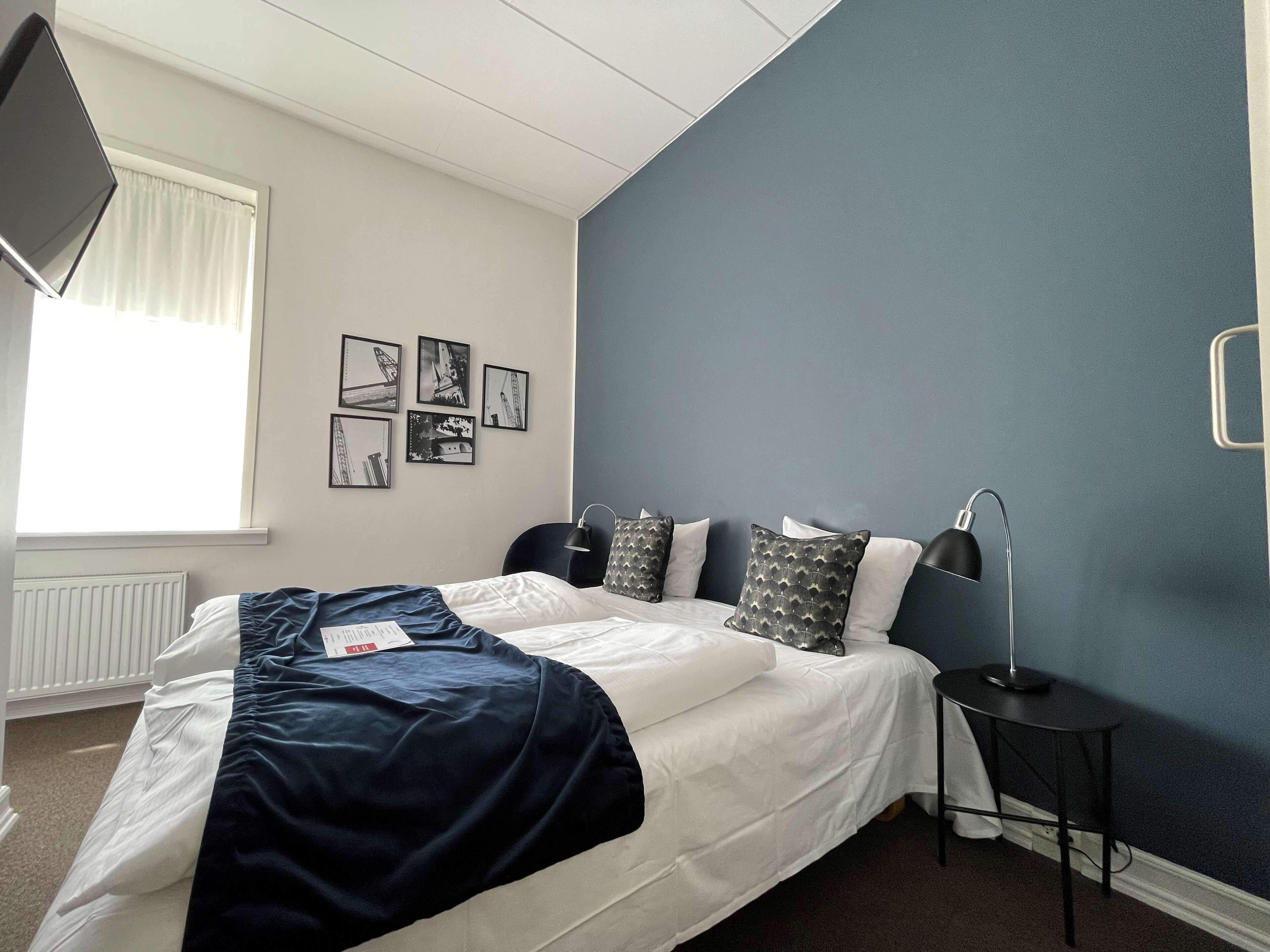 Ein Schlafzimmer mit einem Bett, einem Nachttisch, einer Lampe und einem Fenster mit Vorhängen.