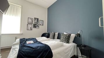 A bedroom with a bed, a nightstand, a lamp, and a window with curtains.
