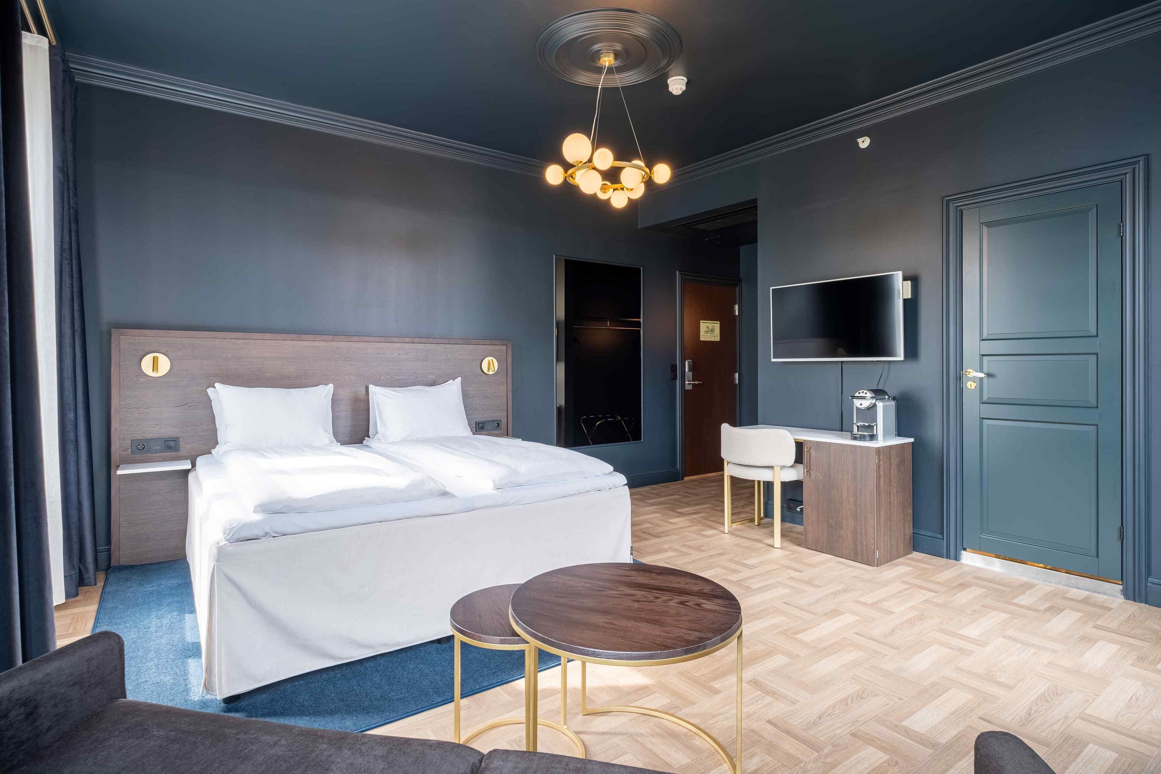 Una habitación de hotel moderna con una cama grande, mesitas de noche, un escritorio, una silla y un televisor.