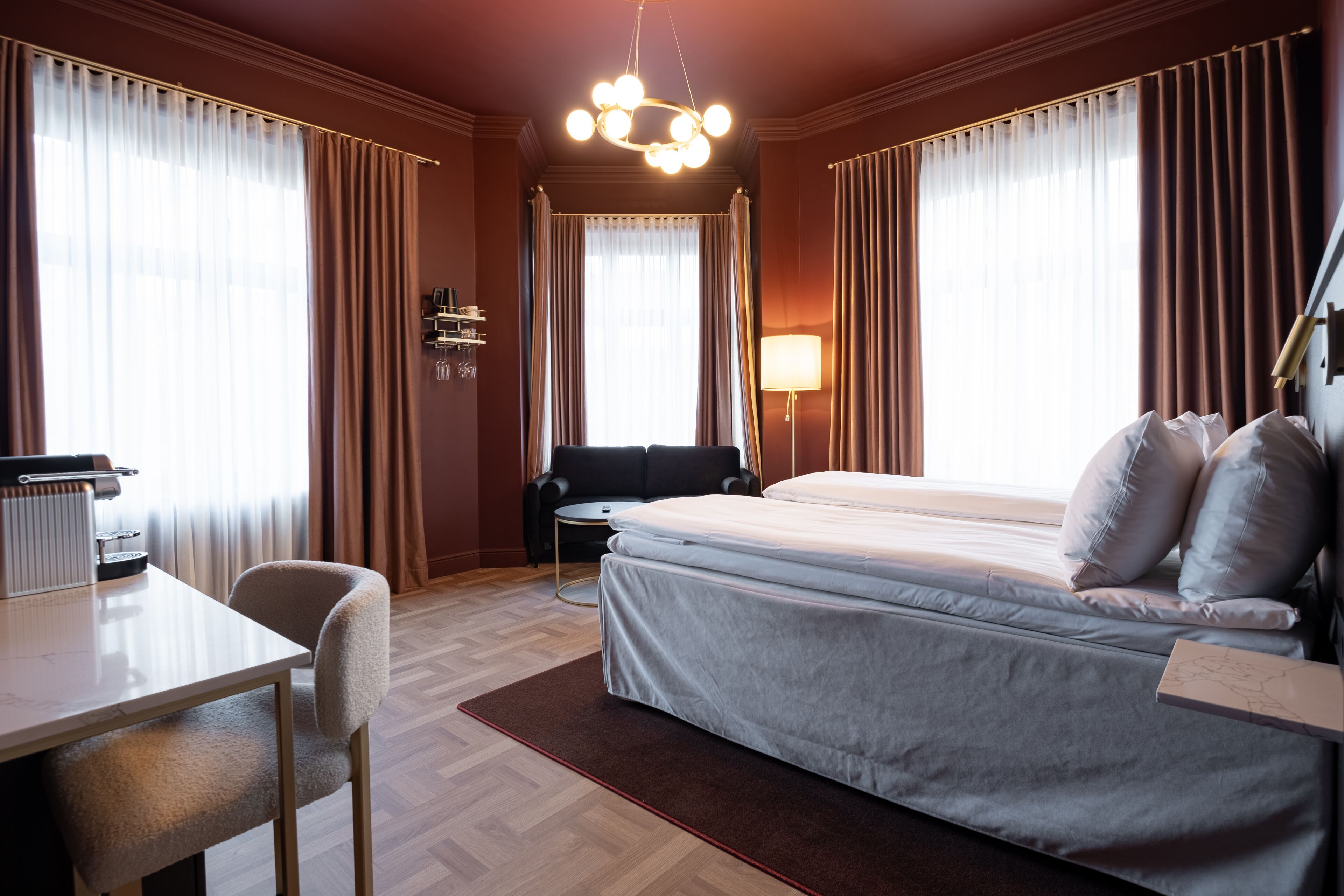 A hotel room with a bed, a desk, a chair, and a lamp.