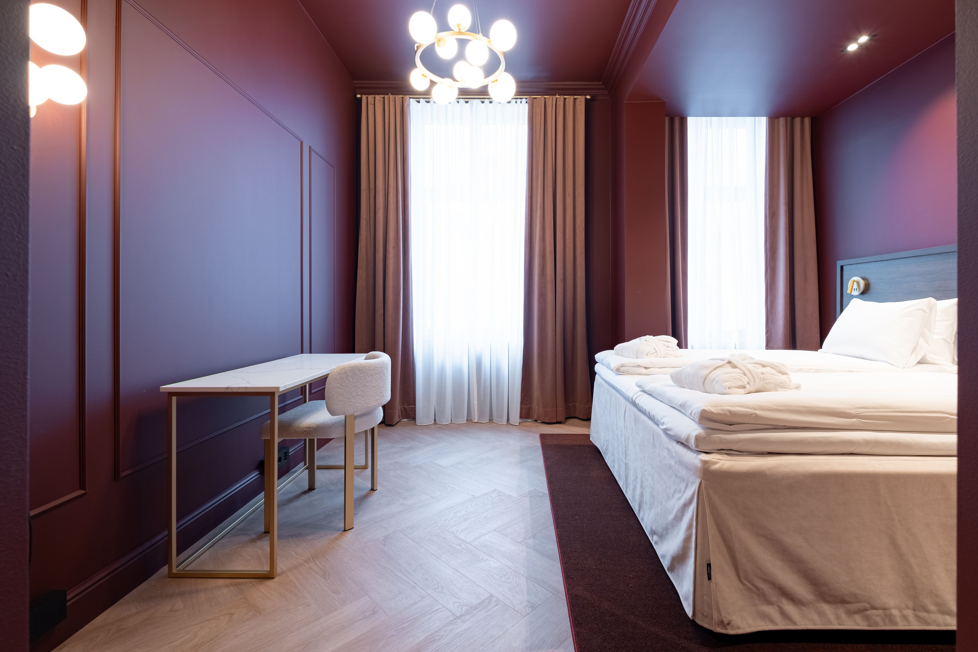 A hotel room with a bed, a desk, a chair, and a large window with curtains.