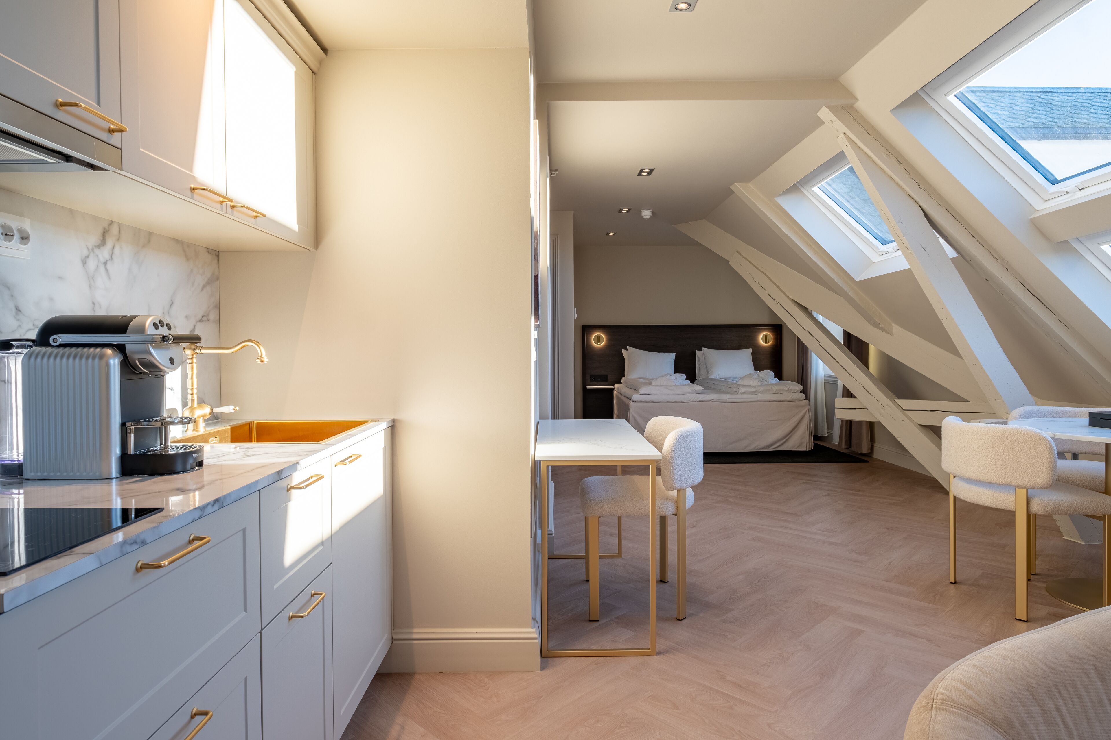 A compact, modern room with a kitchen area, a dining table, and a bedroom with a skylight.