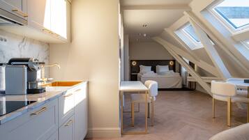 A compact, modern room with a kitchen area, a dining table, and a bedroom with a skylight.