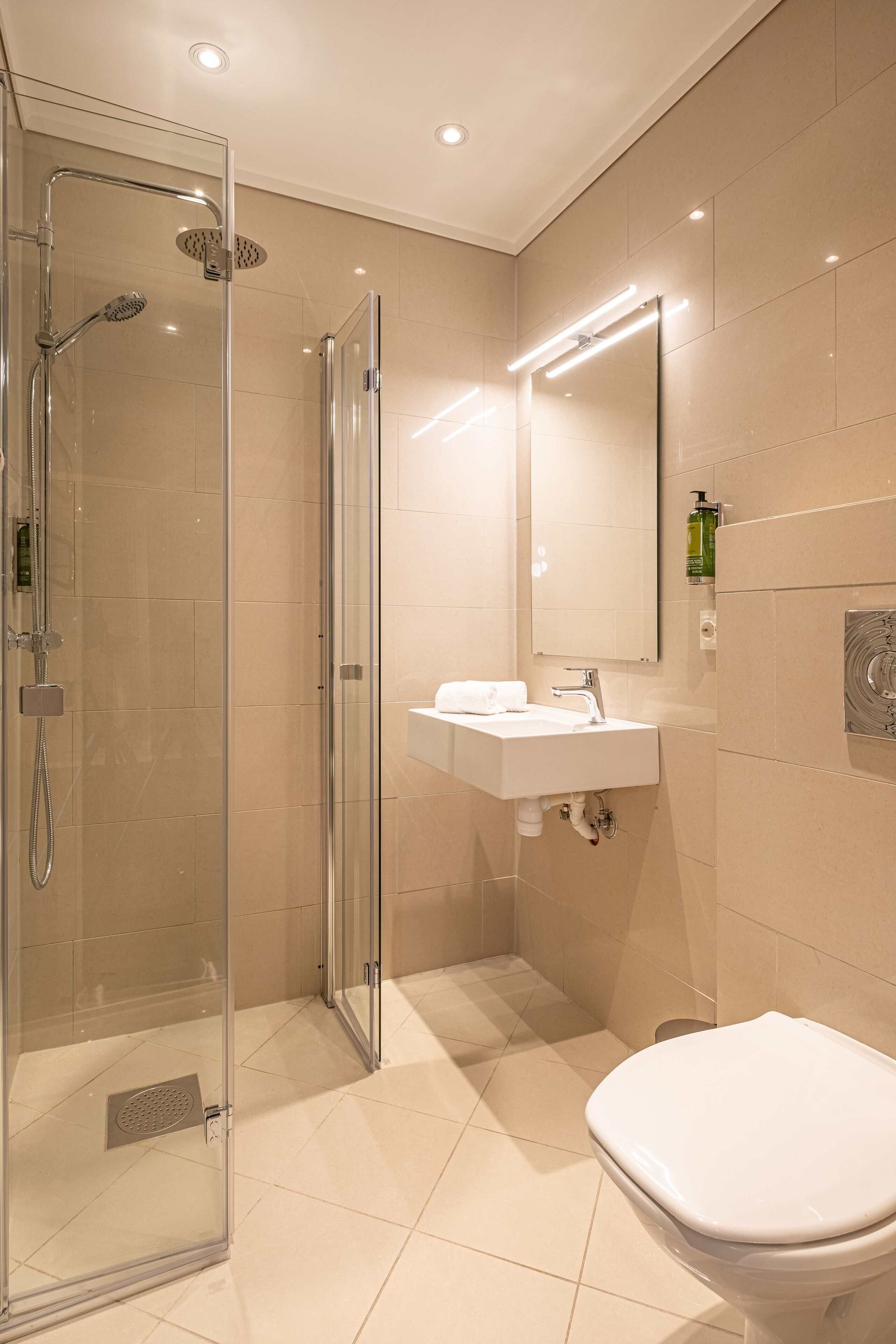 Een moderne badkamer met een glazen douchecabine, een wit wastafelmeubel en een toilet.