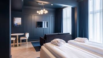 A modern hotel room with a large bed, a flat-screen TV, a small round table with chairs, and a painting on the wall.