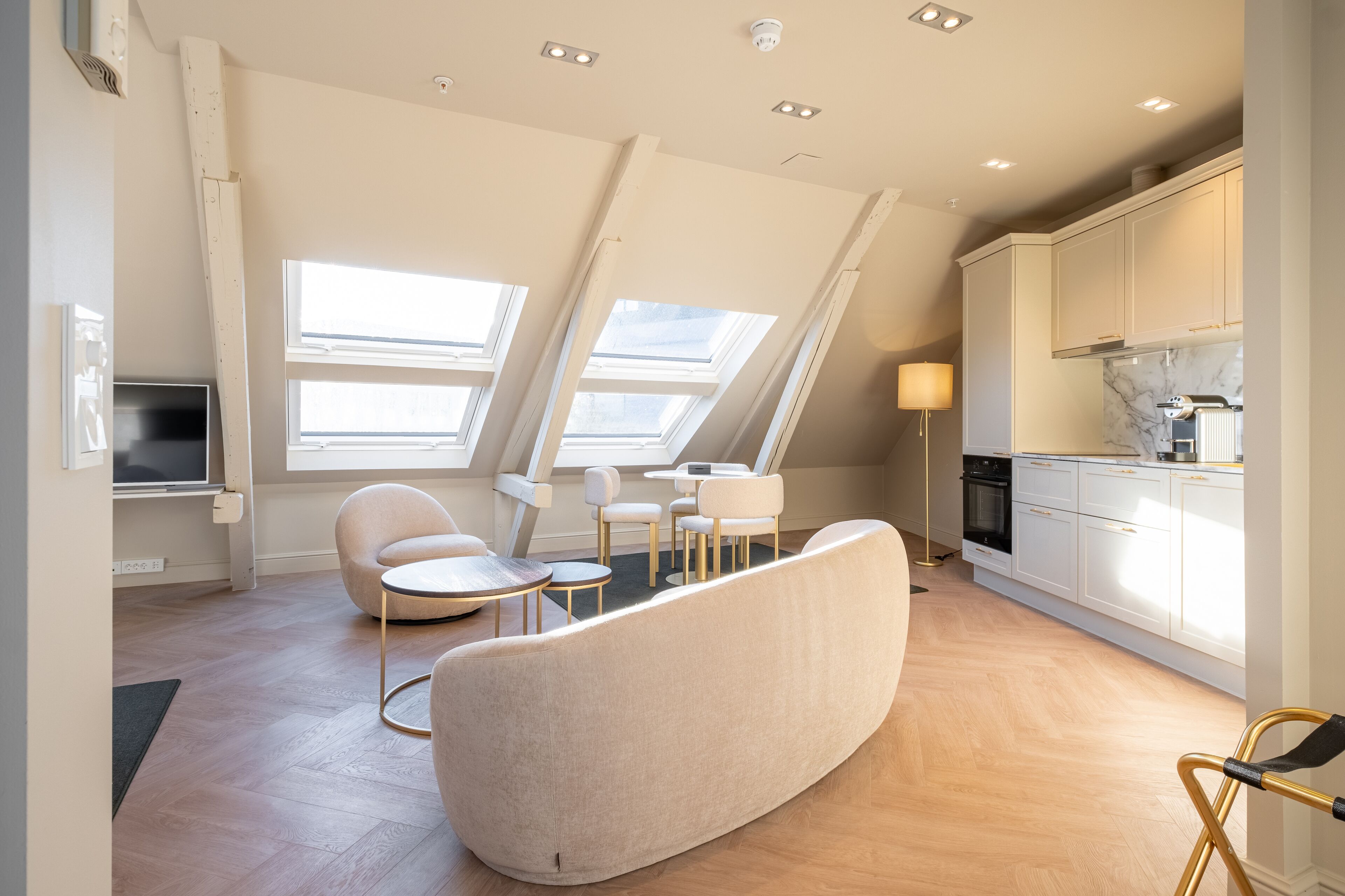 Un appartamento moderno con soffitto a volta, una cucina con mobili bianchi e un'area salotto con un divano curvo e tavoli rotondi.