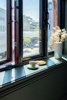Uma janela com vista para um edifício e um vaso com flores no parapeito.