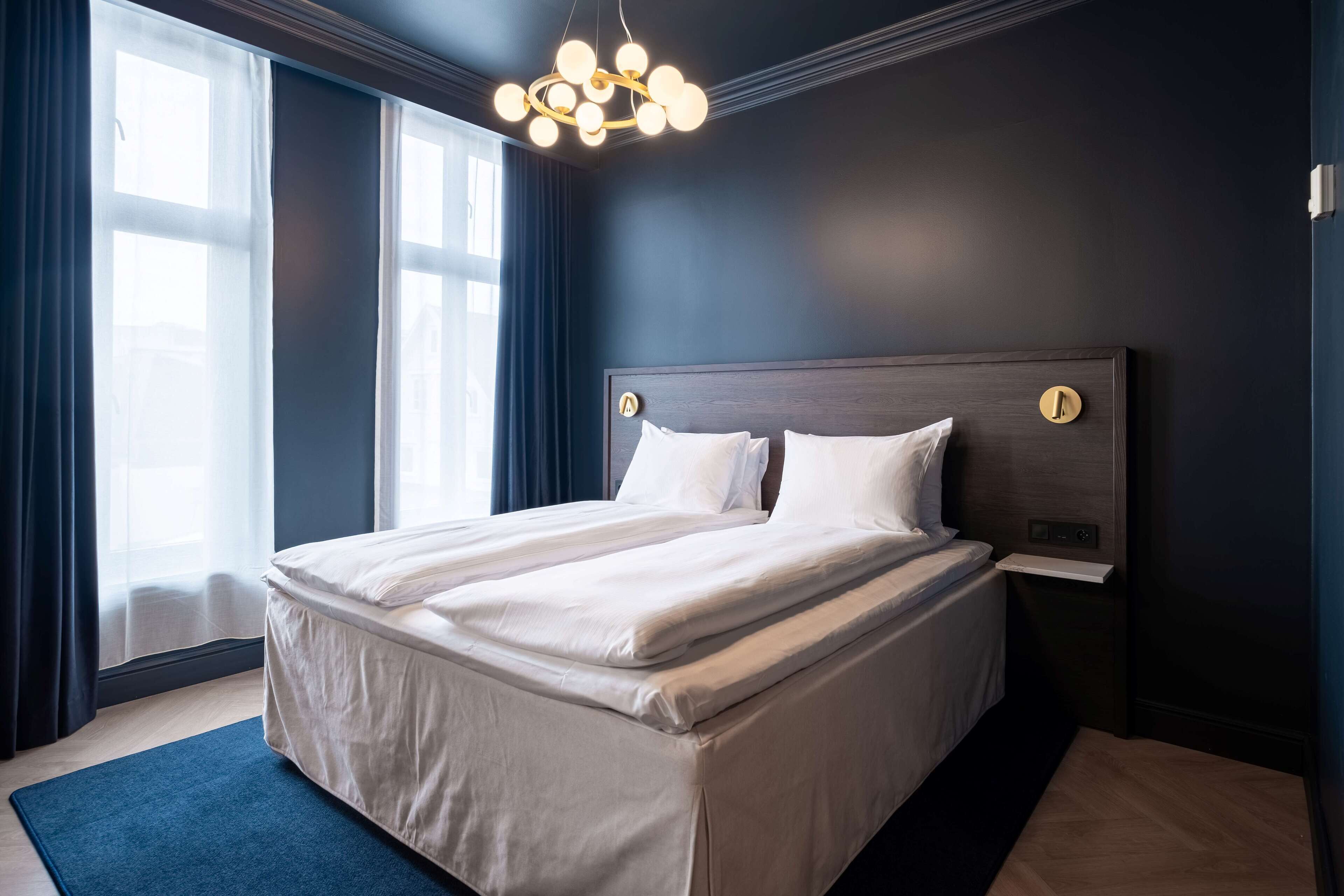 Een moderne hotelkamer met een groot bed, donkere muren en een kroonluchter.
